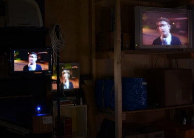 A dark room filled with shelves, three television screens are displaying a talking cartoon of a man. Fine Art Gallery in London. Collectable art in Penge.